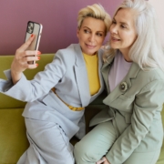 Woman in Gray Blazer Holding Iphone Beside Woman in Green Blazer