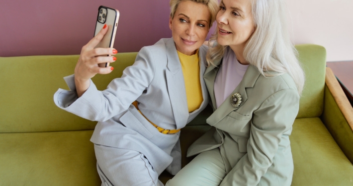 Woman in Gray Blazer Holding Iphone Beside Woman in Green Blazer