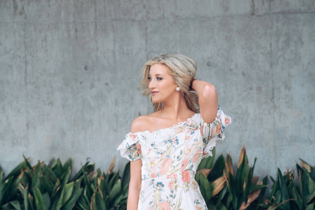 woman in white floral dress standing near gray wall