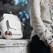 woman wearing beige and red floral top leaning on gray concrete slab with white leather bag ontop