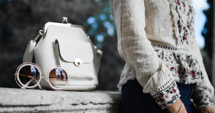 woman wearing beige and red floral top leaning on gray concrete slab with white leather bag ontop