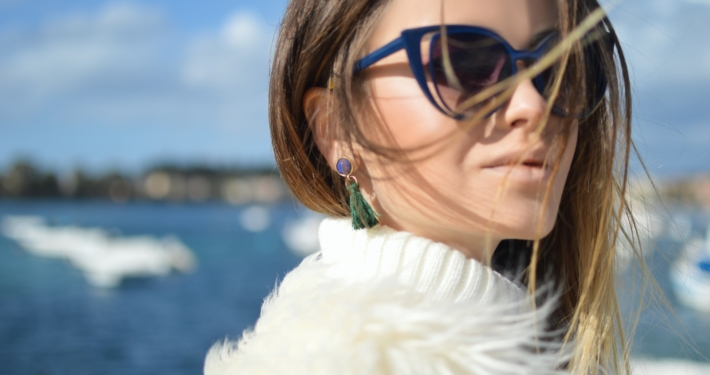 woman wearing blue-framed cat-eye sunglasses with body of water background