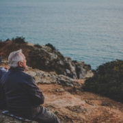 two person sitting on rock staring at body of water during daytime