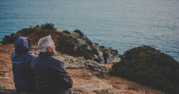 two person sitting on rock staring at body of water during daytime