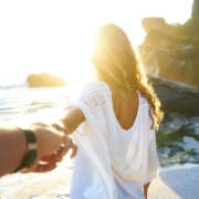 person holding woman's hand beside sea while facing sunlight