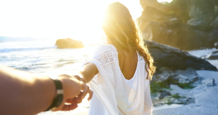 person holding woman's hand beside sea while facing sunlight