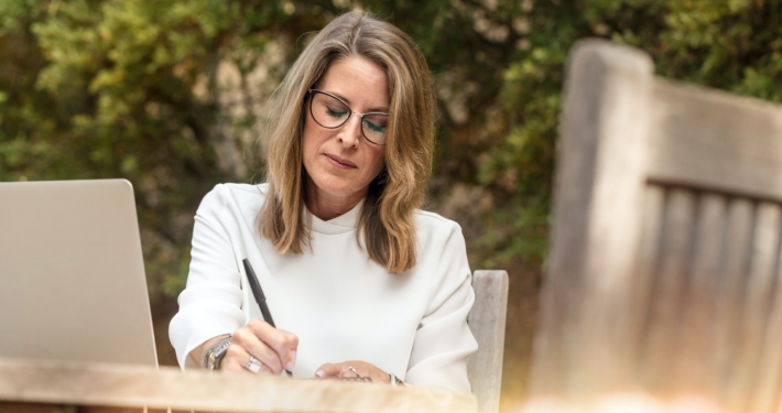 Woman Sitting on Gray Chair While Writing on Table