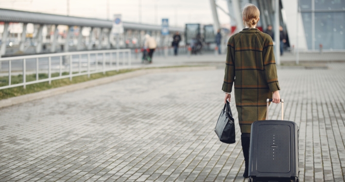 Unrecognizable woman with suitcase walking near airport terminal