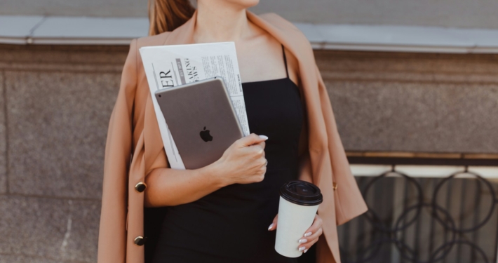 Professional Wardrobe - a woman in a black dress holding a coffee cup and a book - Cosmopolitan Courier