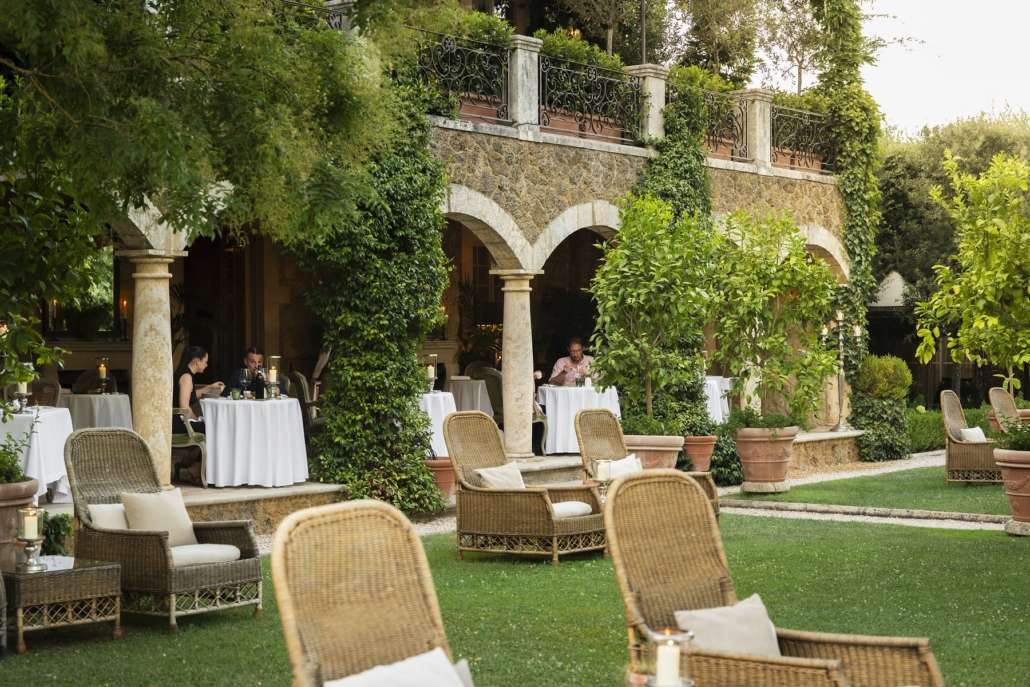 Tables laid beneath the stone arcades, with garden chairs on the lawn.