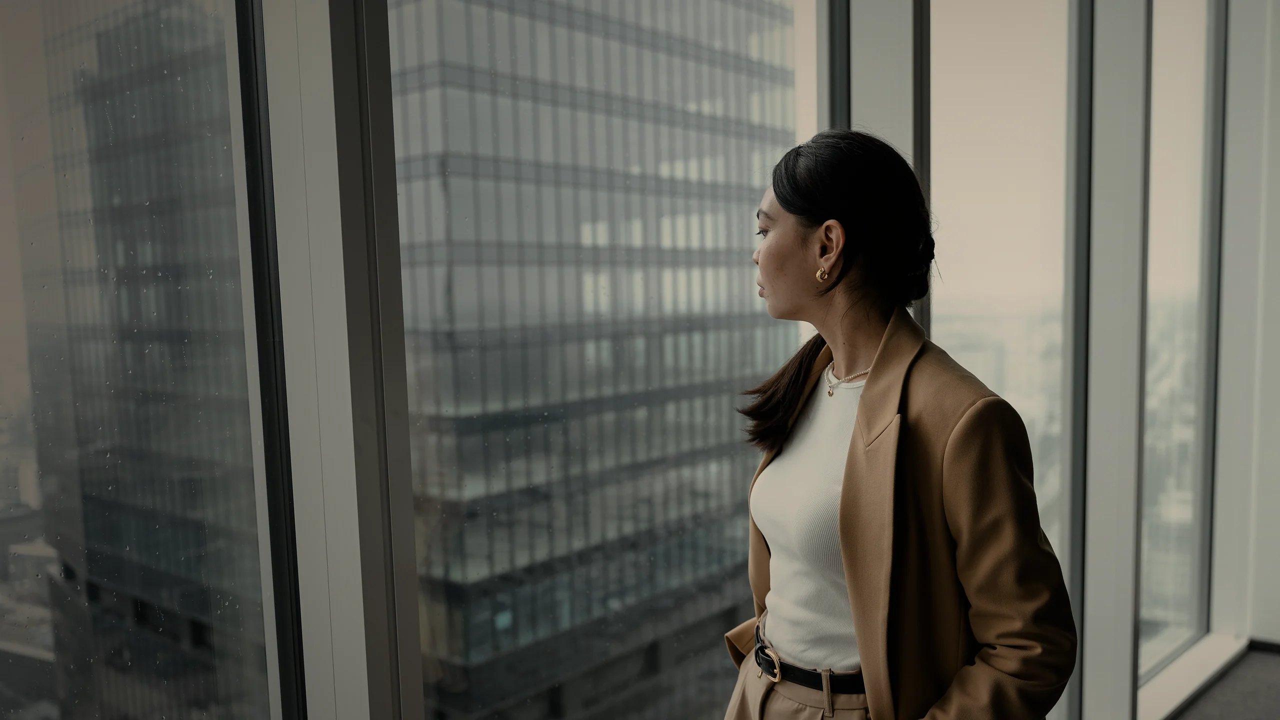 Businesswoman in a camel suit at a high-rise office window, taking in the city’s skyline